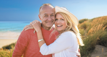 A lady and man are hugging and smiling on the beach.