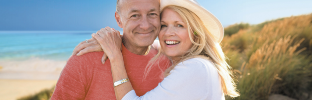 A lady and man are hugging and smiling on the beach.